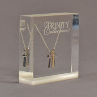 Embedded cross on a chain with product logo Trinity Collection laser engraved on the surface of the acrylic block.